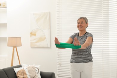 Senior woman doing exercise with fitness elastic band at home. Space for text