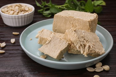 Plate with pieces of tasty halva and peanuts on wooden table, closeup