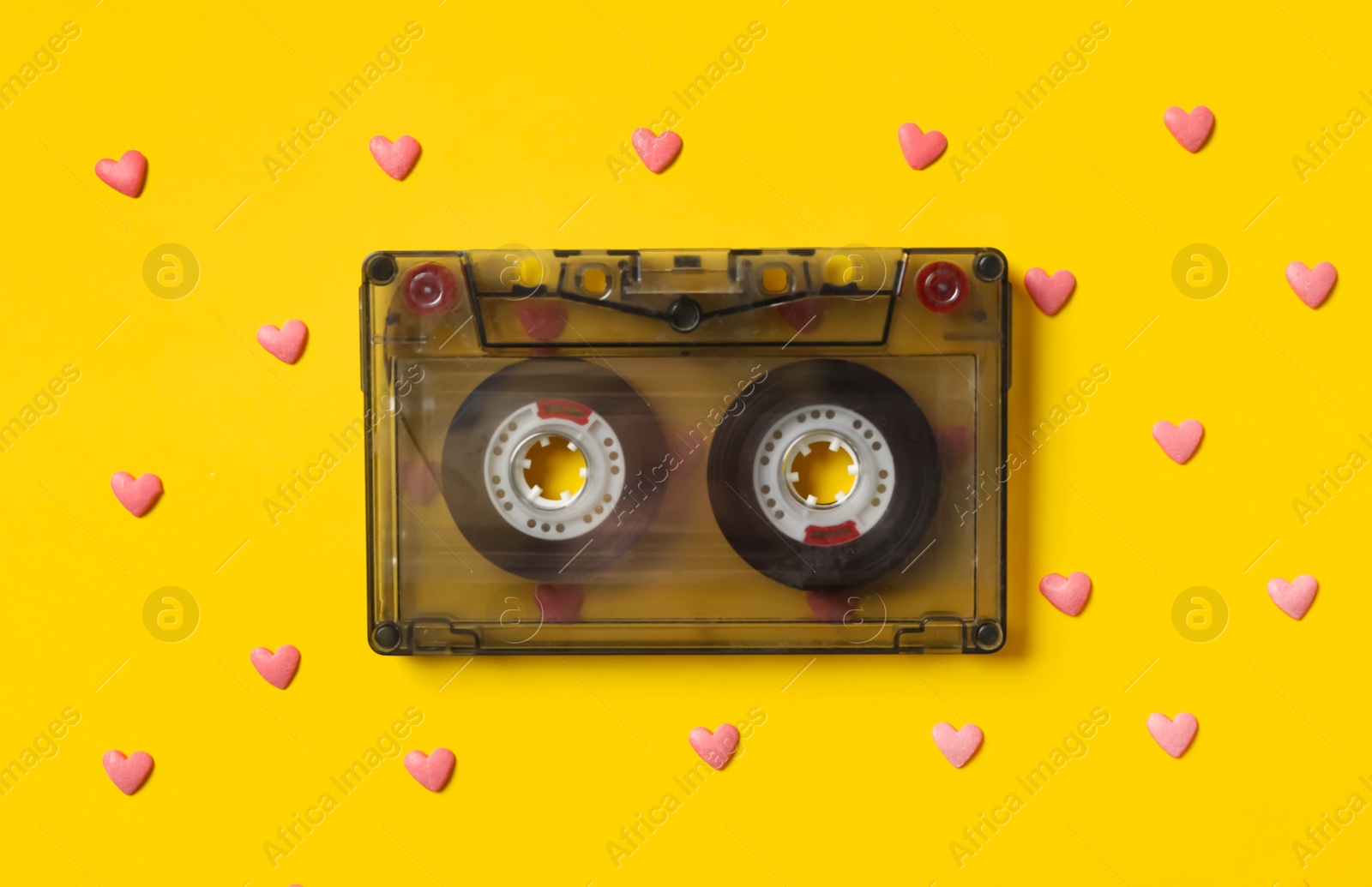 Photo of Music cassette and pink heart shaped sprinkles on yellow background, flat lay. Listening love songs