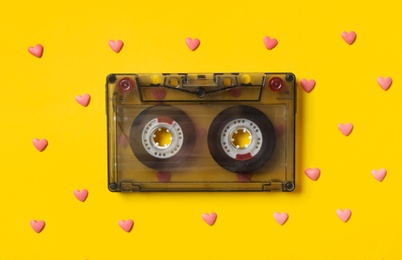 Photo of Music cassette and pink heart shaped sprinkles on yellow background, flat lay. Listening love songs