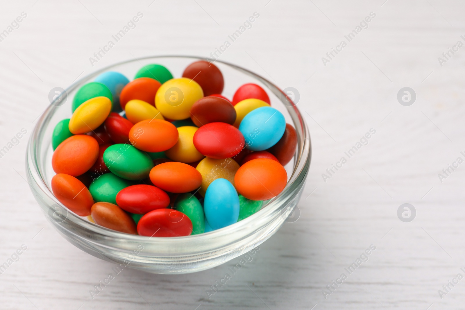 Photo of Bowl with tasty colorful candies on white wooden table, closeup