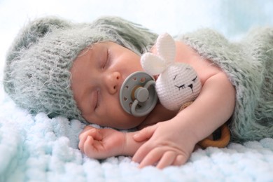 Photo of Cute newborn baby with pacifier sleeping on light blue blanket, closeup