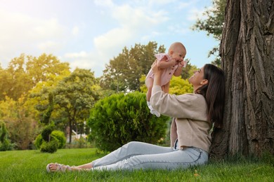 Photo of Happy mother with adorable baby sitting on green grass in park