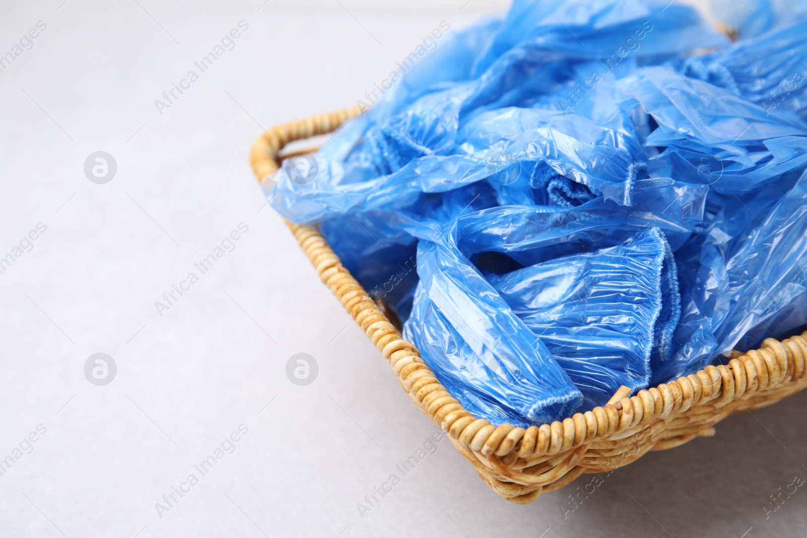 Photo of Blue medical shoe covers in wicker basket on light background, closeup. Space for text