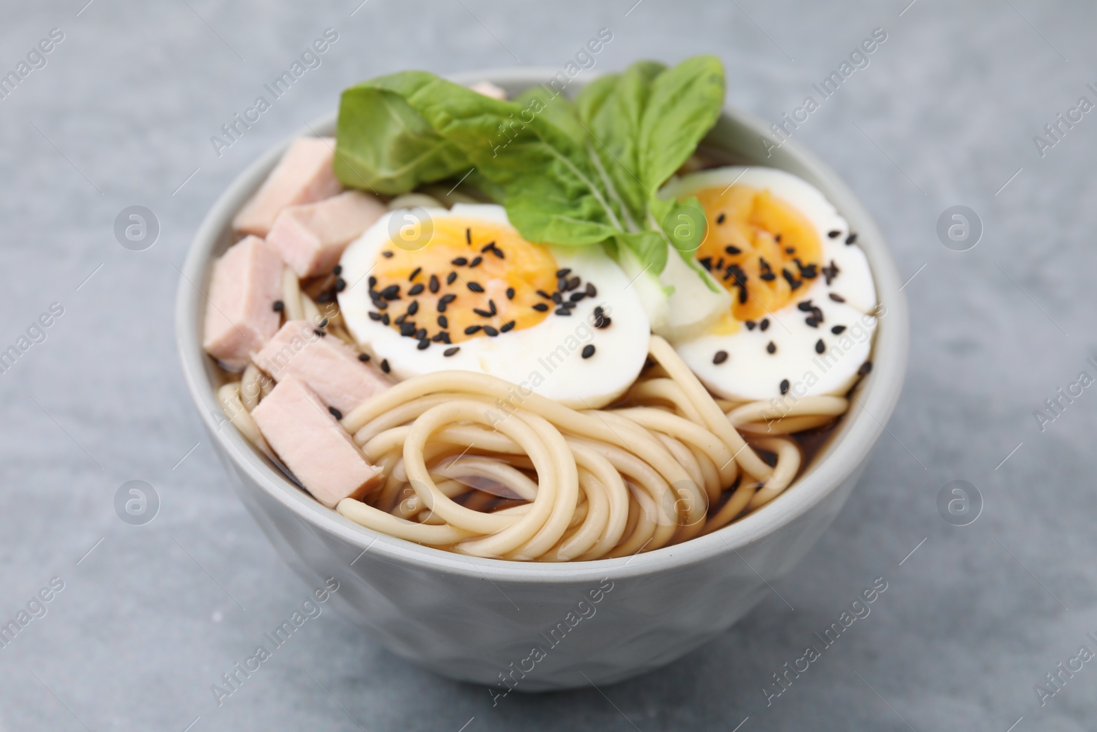 Photo of Bowl of delicious ramen with meat and egg on light grey table, closeup. Noodle soup