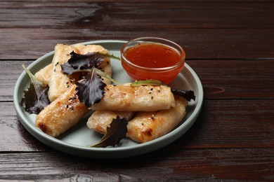 Photo of Tasty fried spring rolls, lettuce and sauce on wooden table