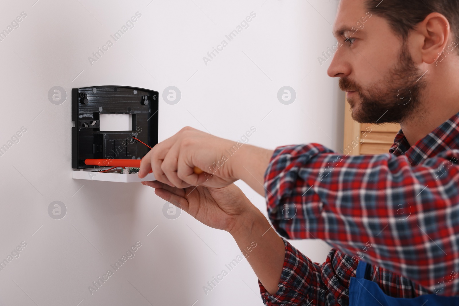 Photo of Technician installing home security alarm system on white wall indoors