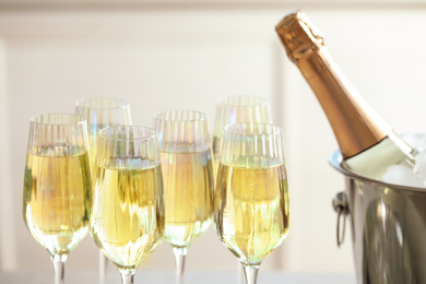 Glasses of champagne and ice bucket with bottle on blurred background