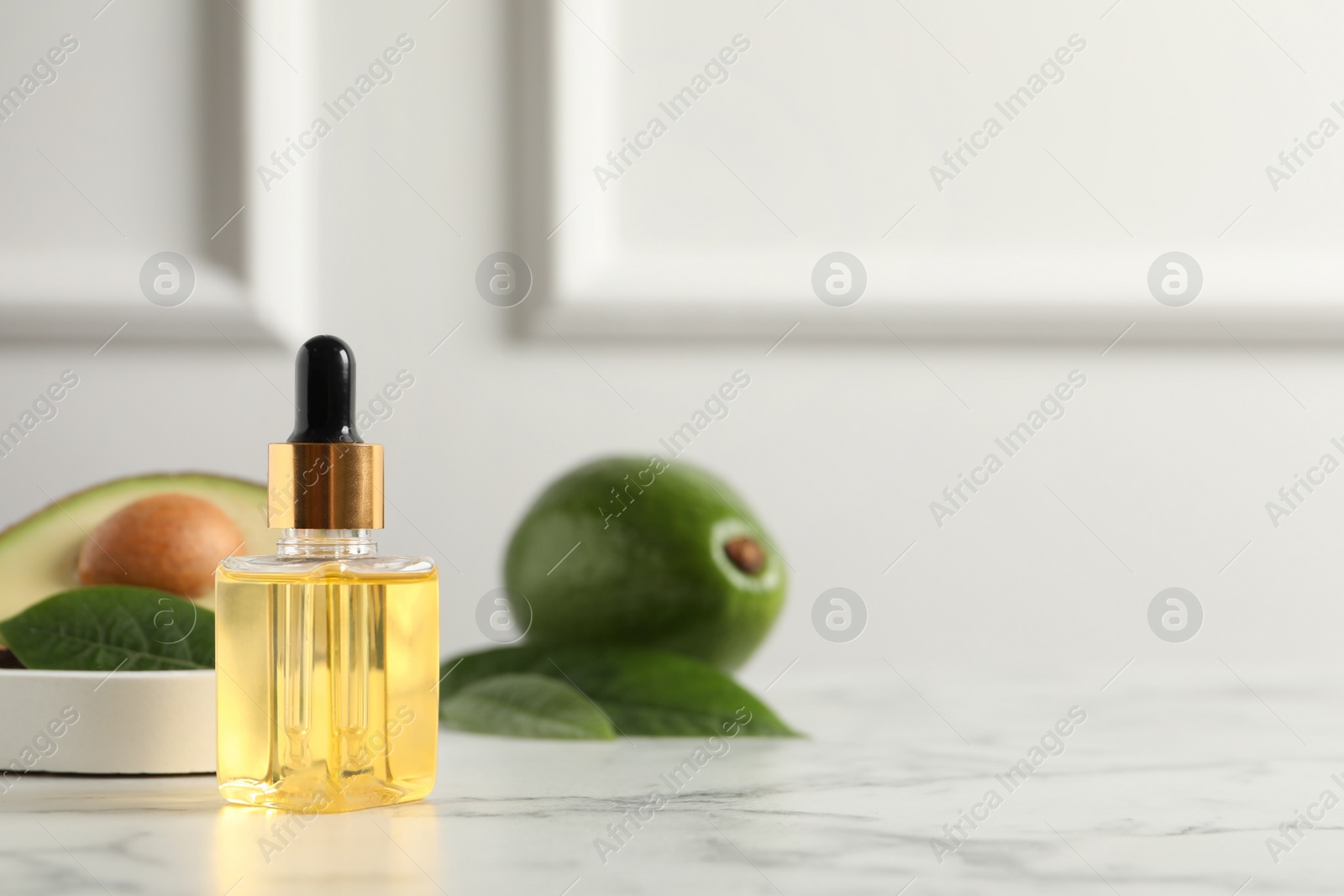 Photo of Bottle of essential oil and avocados on white marble table, space for text