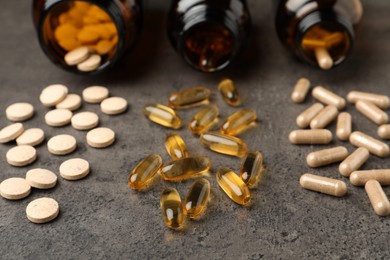 Overturned bottles with different dietary supplements on grey table, closeup