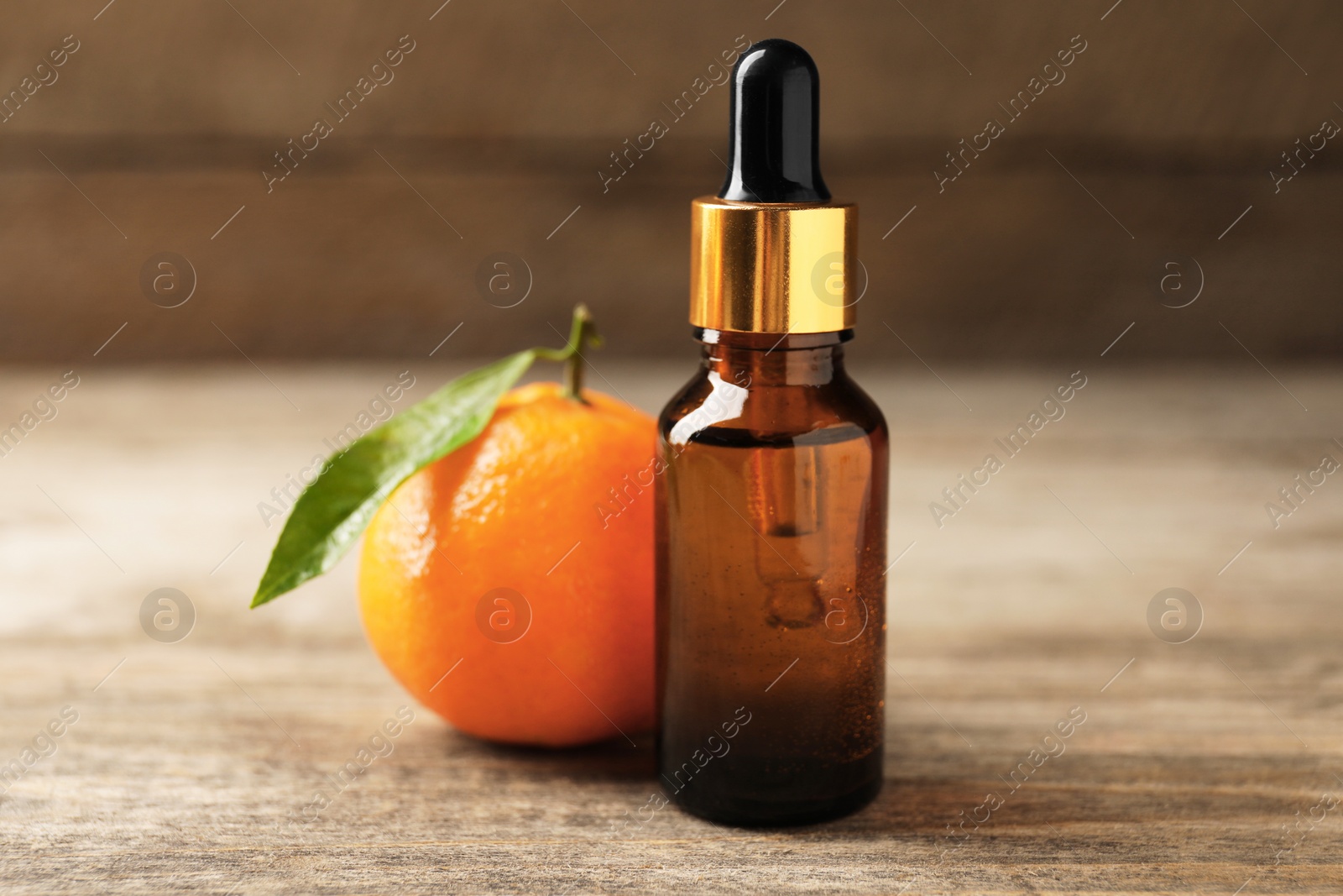 Photo of Bottle of tangerine essential oil and fresh fruit on wooden table, closeup
