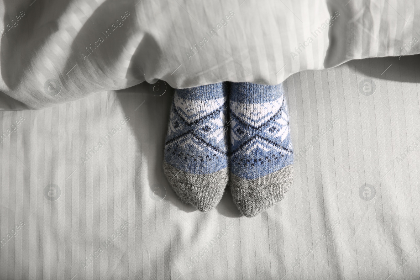 Photo of Woman wearing knitted socks under blanket in bed, top view