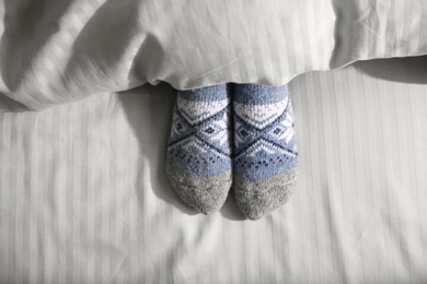 Photo of Woman wearing knitted socks under blanket in bed, top view