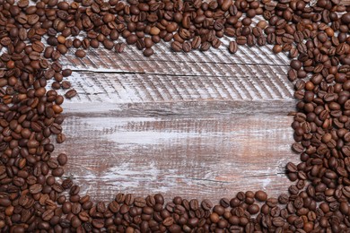 Photo of Frame of roasted coffee beans on wooden table, flat lay. Space for text