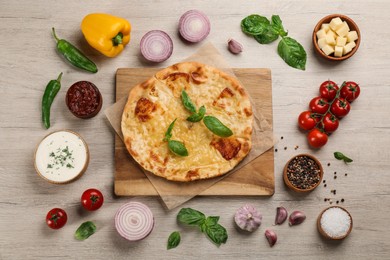 Photo of Delicious khachapuri with cheese, sauces, vegetables and spices on wooden table, flat lay