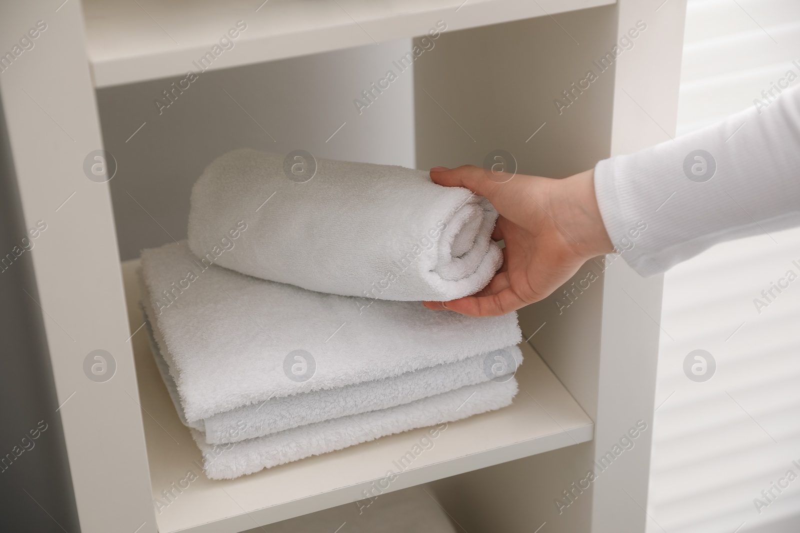 Photo of Woman stacking clean towels on shelf in bathroom, closeup