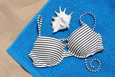 Photo of Blue beach towel, seashell and swimsuit on sand, top view