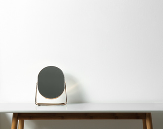 Photo of Small mirror on table near white wall. Space for text