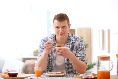 Photo of Young man spreading jam onto tasty toasted bread at table
