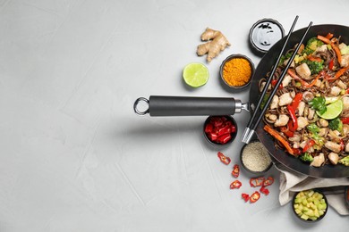 Photo of Stir-fry. Tasty noodles with meat in wok, chopsticks and ingredients on grey textured table, flat lay. Space for text