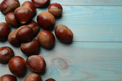 Photo of Roasted edible sweet chestnuts on light blue wooden table, flat lay. Space for text