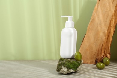Photo of Bottle of cosmetic product with olive essential oil on stone with moss against light green background. Space for text