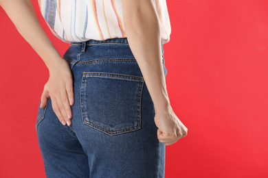 Photo of Woman suffering from hemorrhoid on red background, closeup
