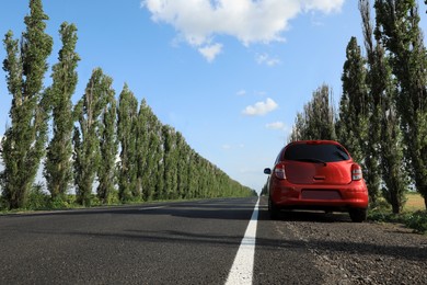 Photo of Red car parked near asphalt road in countryside