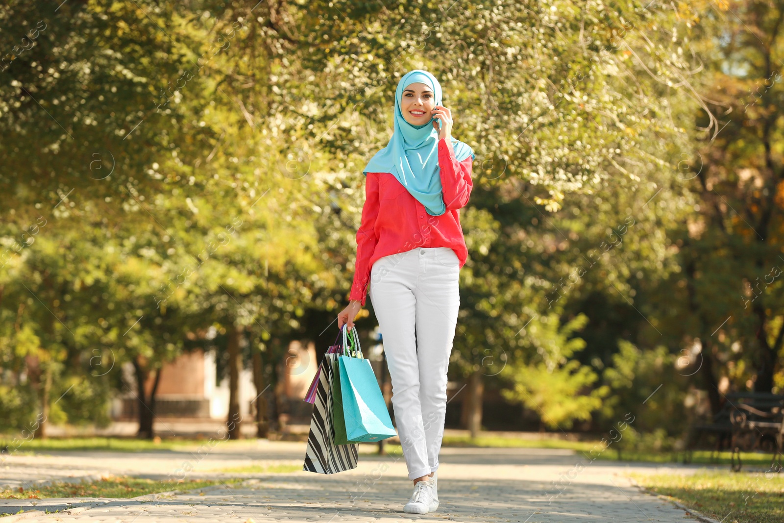 Photo of Muslim woman with shopping bags talking on phone in park