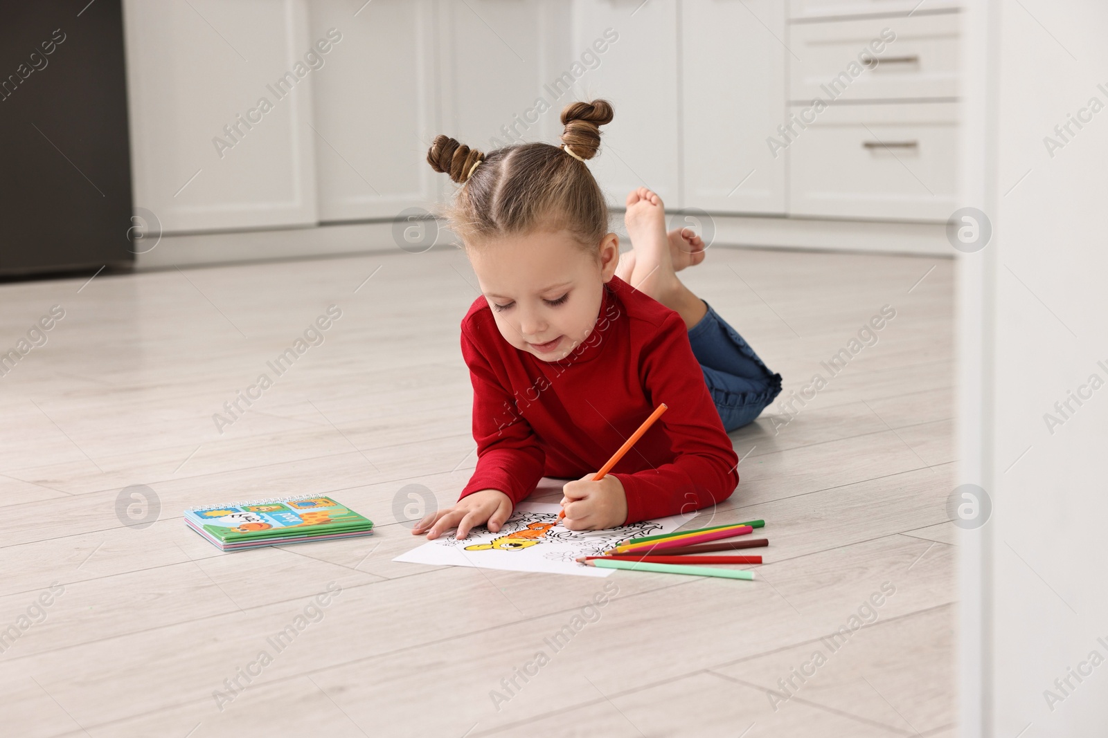 Photo of Cute little girl coloring drawing on warm floor in kitchen. Heating system