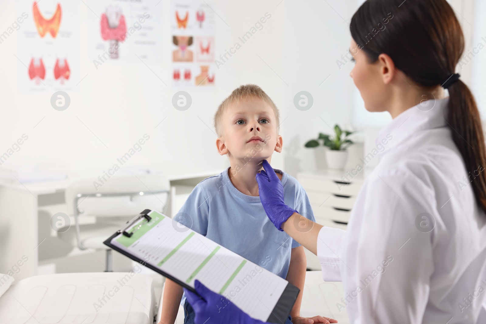 Photo of Endocrinologist with clipboard examining boy's thyroid gland at hospital