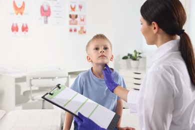 Endocrinologist with clipboard examining boy's thyroid gland at hospital