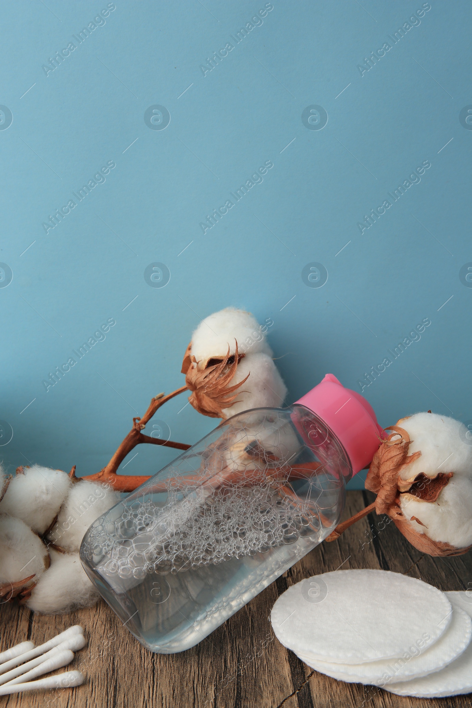 Photo of Composition with makeup remover and cotton flowers on wooden table against light blue background, space for text