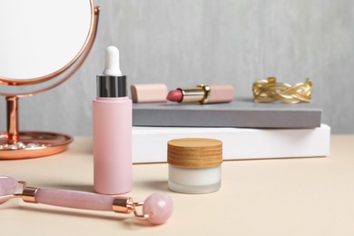 Photo of Facial roller and cosmetic products on beige dressing table