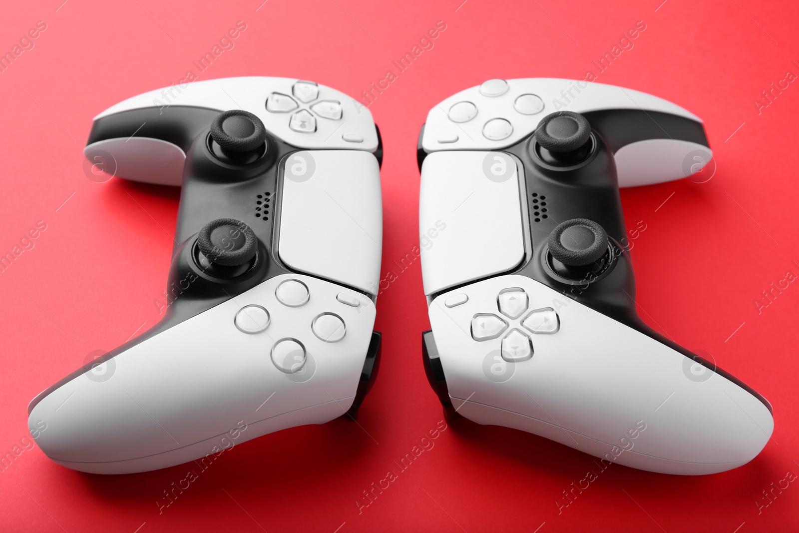 Photo of Two wireless game controllers on red background, closeup