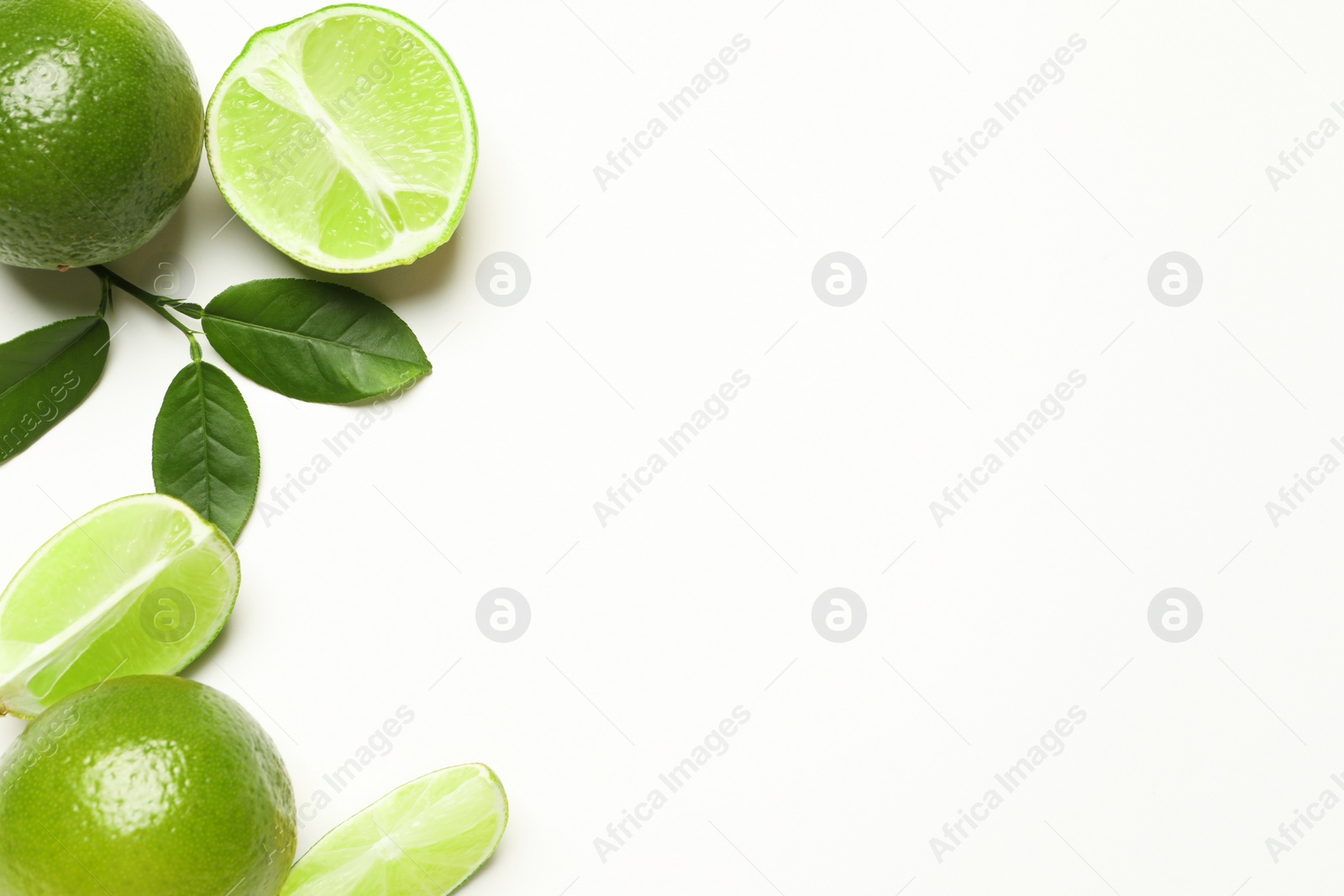 Photo of Whole and cut fresh ripe limes with green leaves on white background, flat lay