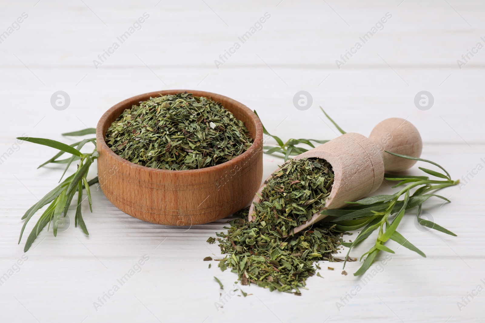 Photo of Bowl of dry tarragon, scoop and fresh leaves on white wooden table