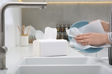 Photo of Woman wiping plate with paper towel above sink in kitchen, closeup