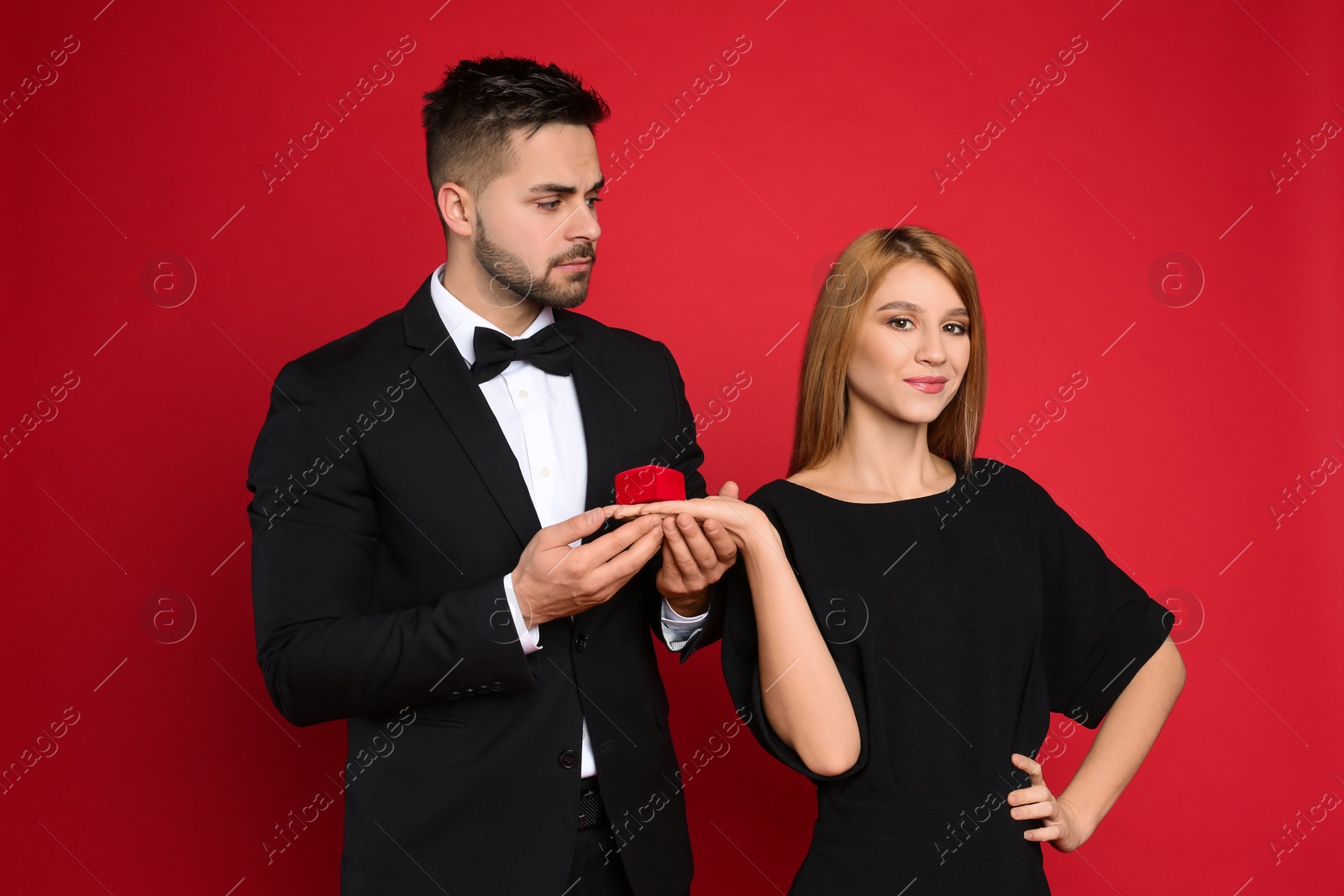 Photo of Young woman with engagement ring making marriage proposal to her boyfriend on red background