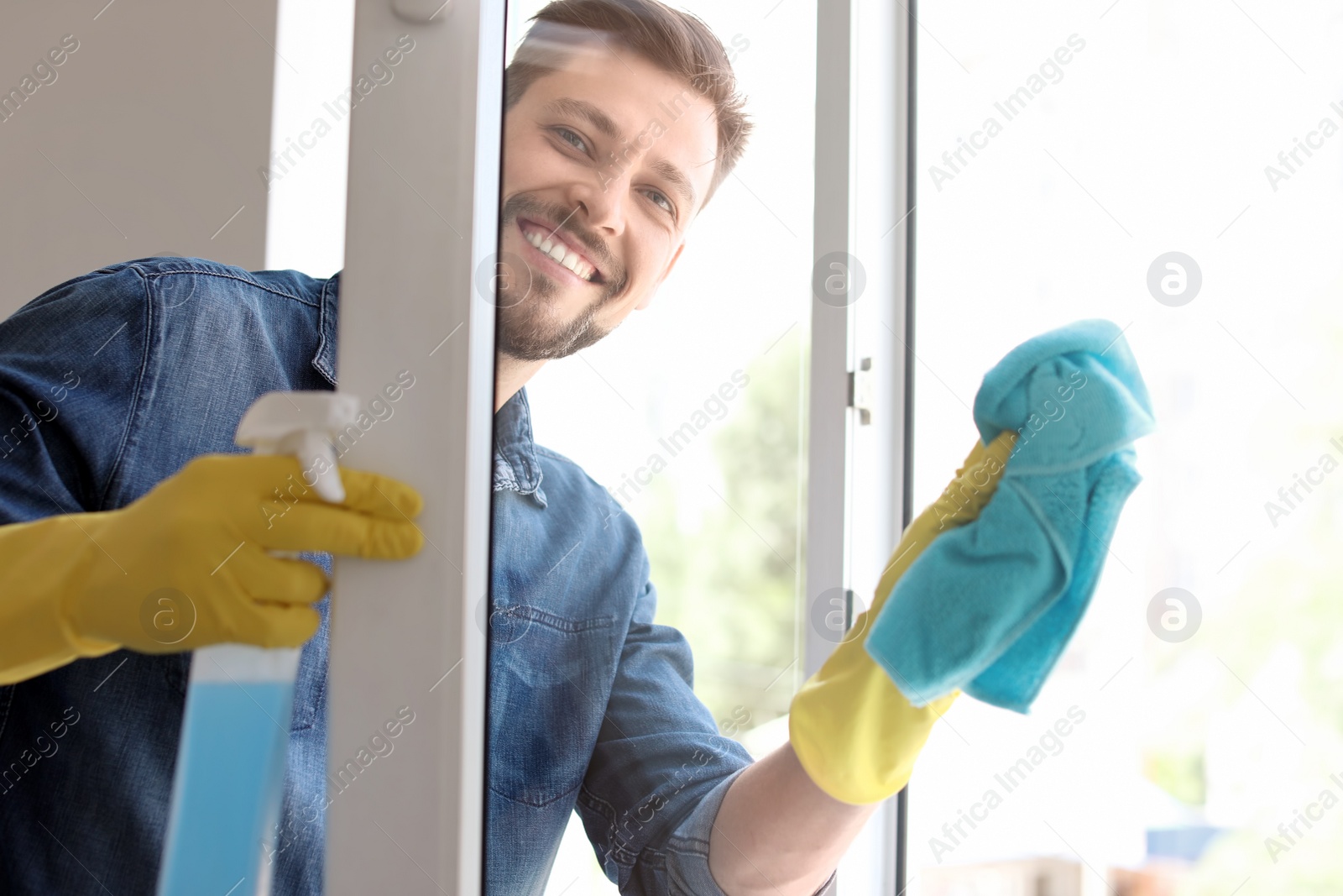 Photo of Man in casual clothes washing window glass at home