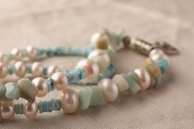 Photo of Beautiful necklace with gemstones on light cloth, closeup