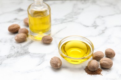 Photo of Bottle and bowl of nutmeg oil, nuts on white marble table