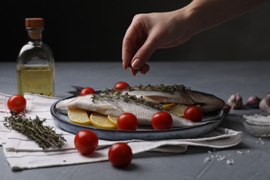 Woman adding spices onto raw dorado fish at grey table, closeup