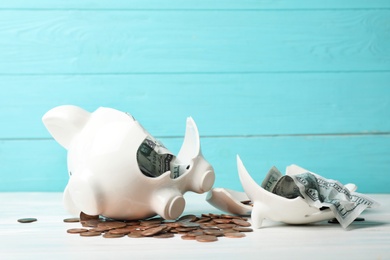 Broken piggy bank with coins and banknotes on wooden table