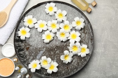 Photo of Bowl of water with flowers and different spa supplies on light grey table, flat lay