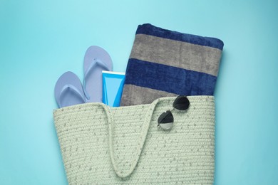 Photo of Beach bag with towel, flip flops, sunglasses and sun protection product on light blue background, top view