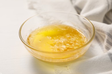 Photo of Melted butter in glass bowl on white wooden table, closeup