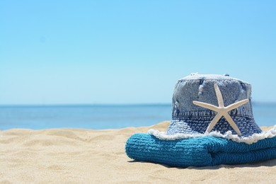 Photo of Stylish denim hat, towel and starfish on sand near sea, space for text. Beach accessories