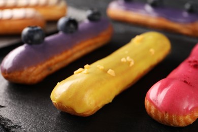 Different tasty glazed eclairs on dark table, closeup