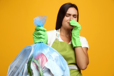 Photo of Woman holding full garbage bag against yellow background, focus on hand